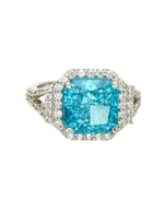 Ring with a large blue gemstone and diamond-studded halo on a white background