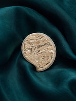 Small embossed gold-tone kumkum box with floral medallion design and curved base