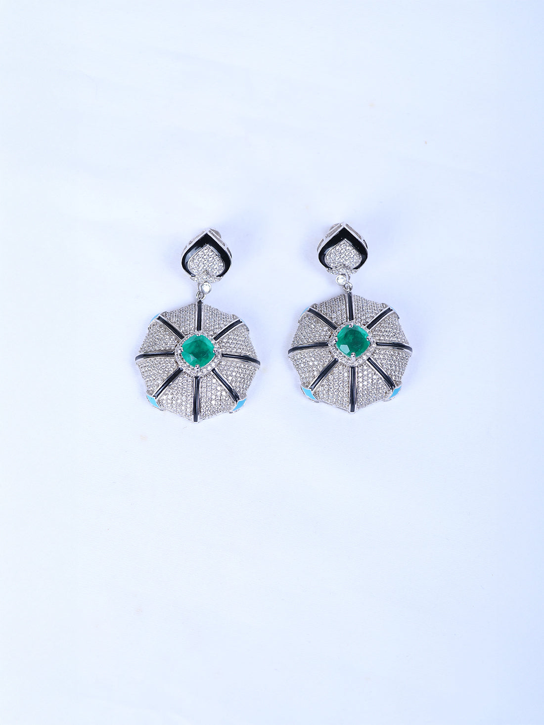 Shop a pair of silver drop earrings with a central green emerald and a small light blue stone at the base.