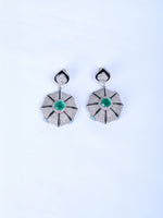 Shop a pair of silver drop earrings with a central green emerald and a small light blue stone at the base.