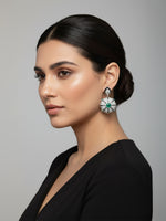 Shop worn silver drop earrings featuring a flower-shaped pave setting with a central green emerald and a small light blue stone at the base.