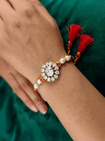 Crystal blossom rakhi with pearl beads and red tassels, worn on a wrist
