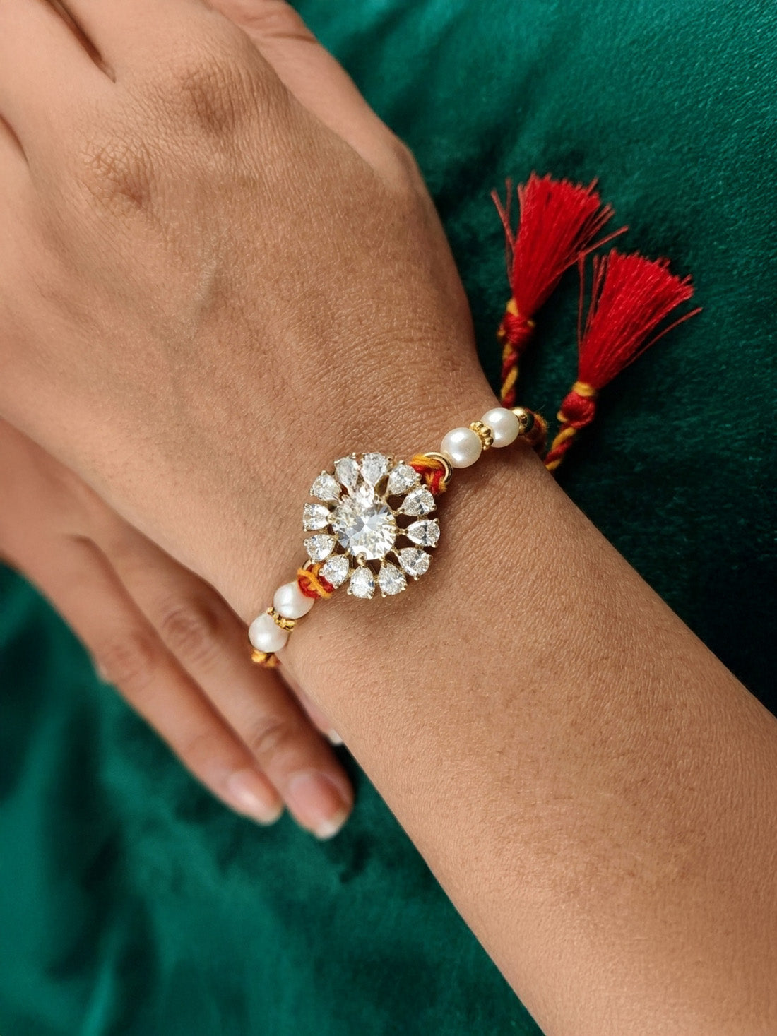 Crystal blossom rakhi with pearl beads and red tassels, worn on a wrist