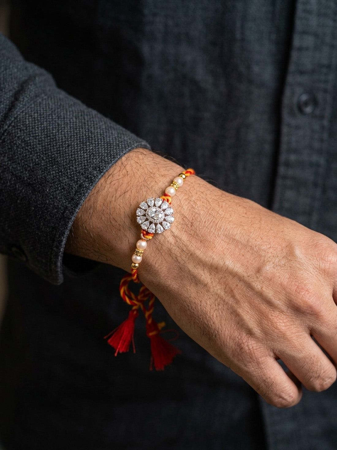 Crystal cluster rakhi with pearl and gold-tone beads and red tassel accents, worn on wrist