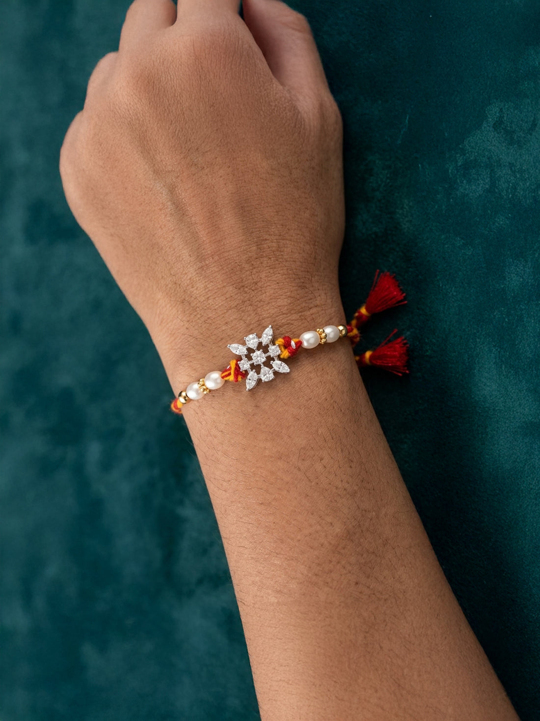 Sterling silver floral rakhi with pearl beads on wrist, red-yellow braided thread