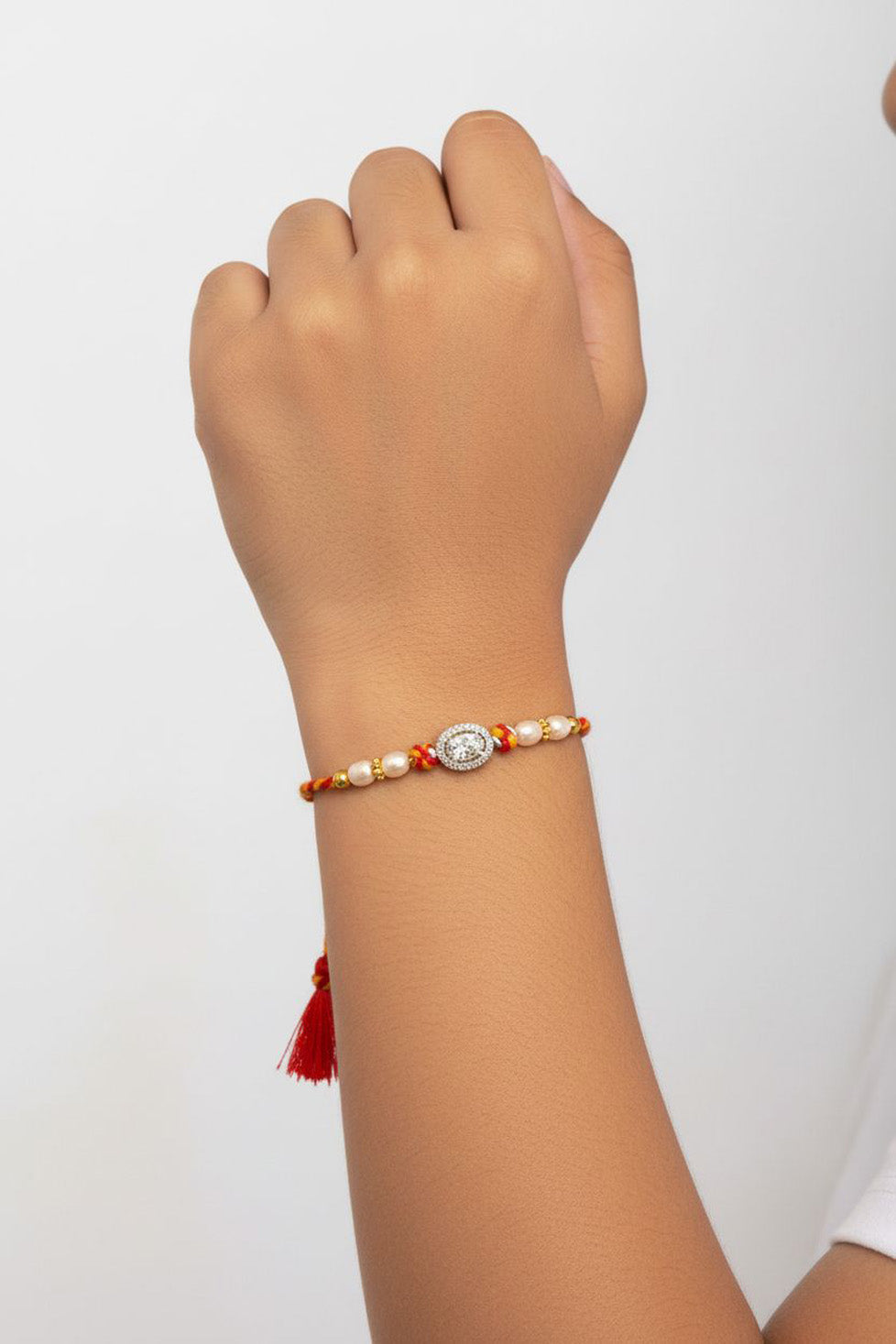Sterling silver oval rakhi charm with pearl beads on red-orange thread on wrist