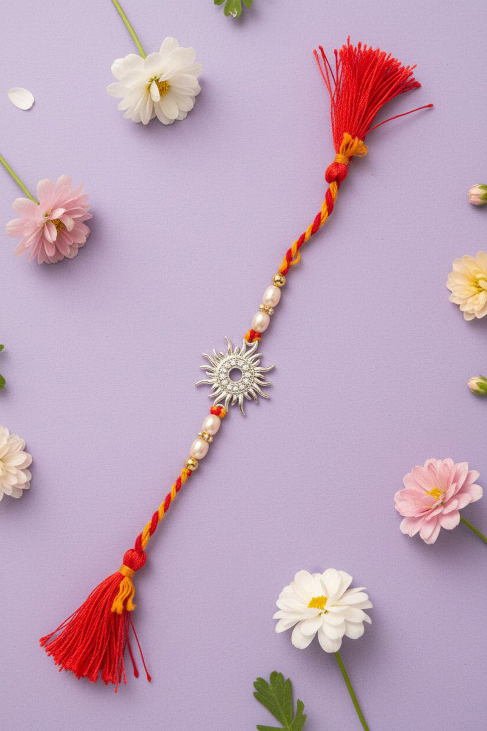 Red and yellow braided rakhi with silver sun charm, pearl beads, and red tassels