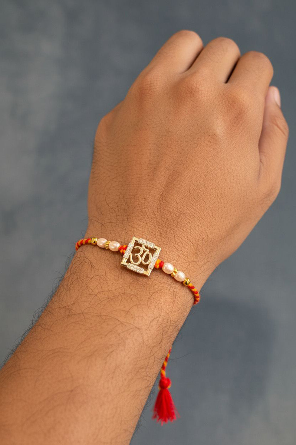 Sterling silver Om square rakhi on wrist with pearl beads and red tassel