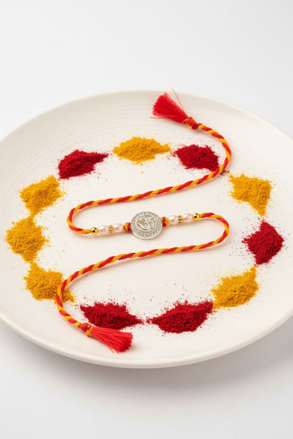 Silver round charm rakhi with pearl beads on braided red-yellow thread, on plate
