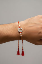 Rakhi on wrist: round silver charm with pearl beads and red tassels on braided cord