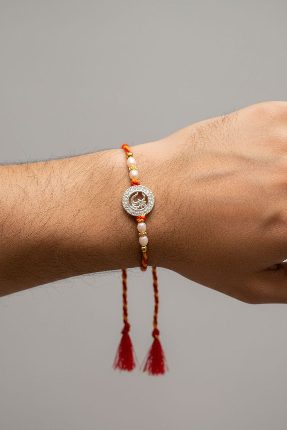 Rakhi on wrist: round silver charm with pearl beads and red tassels on braided cord