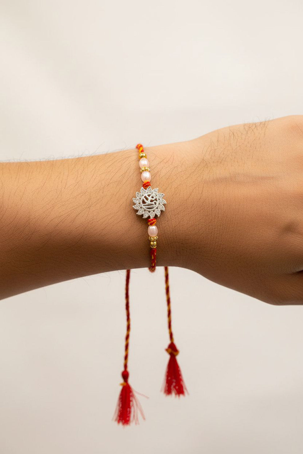 Sterling silver rakhi bracelet with filigree charm, red tassels, and gold bead accents