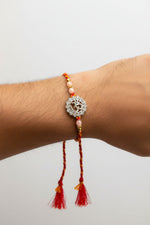 Sterling silver rakhi bracelet on wrist: round filigree pendant, pearl beads, red tassels