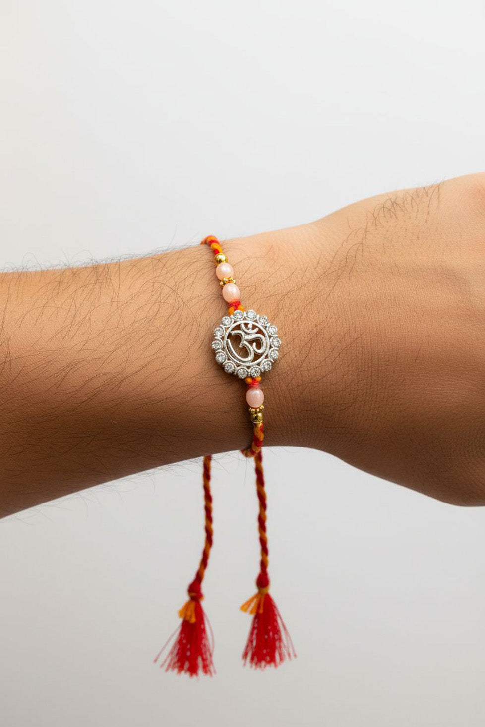 Sterling silver rakhi bracelet on wrist: round filigree pendant, pearl beads, red tassels