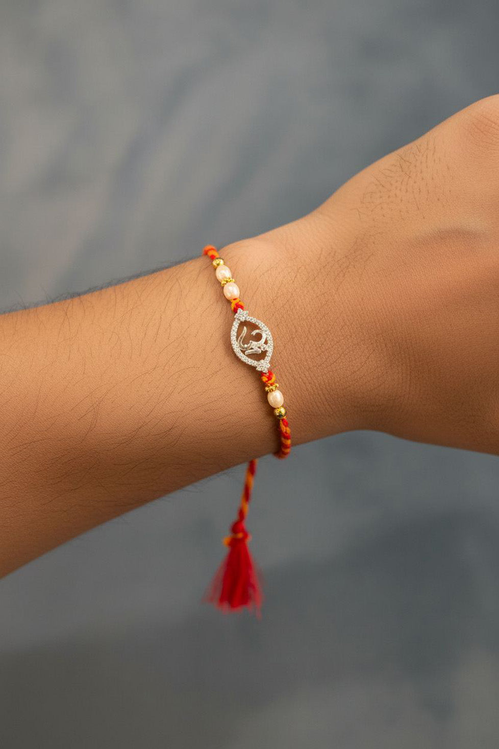 Sterling silver Om rakhi on wrist, red-yellow striped thread with pearl beads and tassel