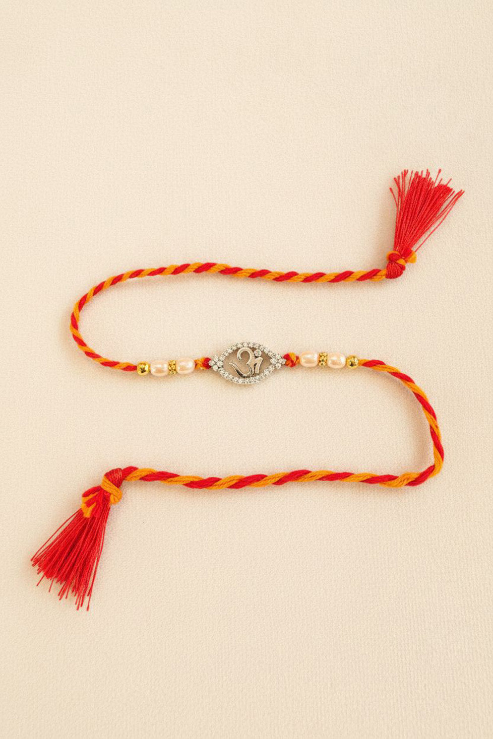 Sterling silver Om rakhi with pearl beads, red-yellow striped thread and tassels