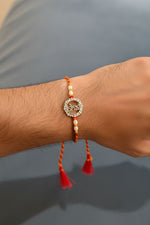 Silver rakhi bracelet with pearl beads and red tassels, worn on wrist