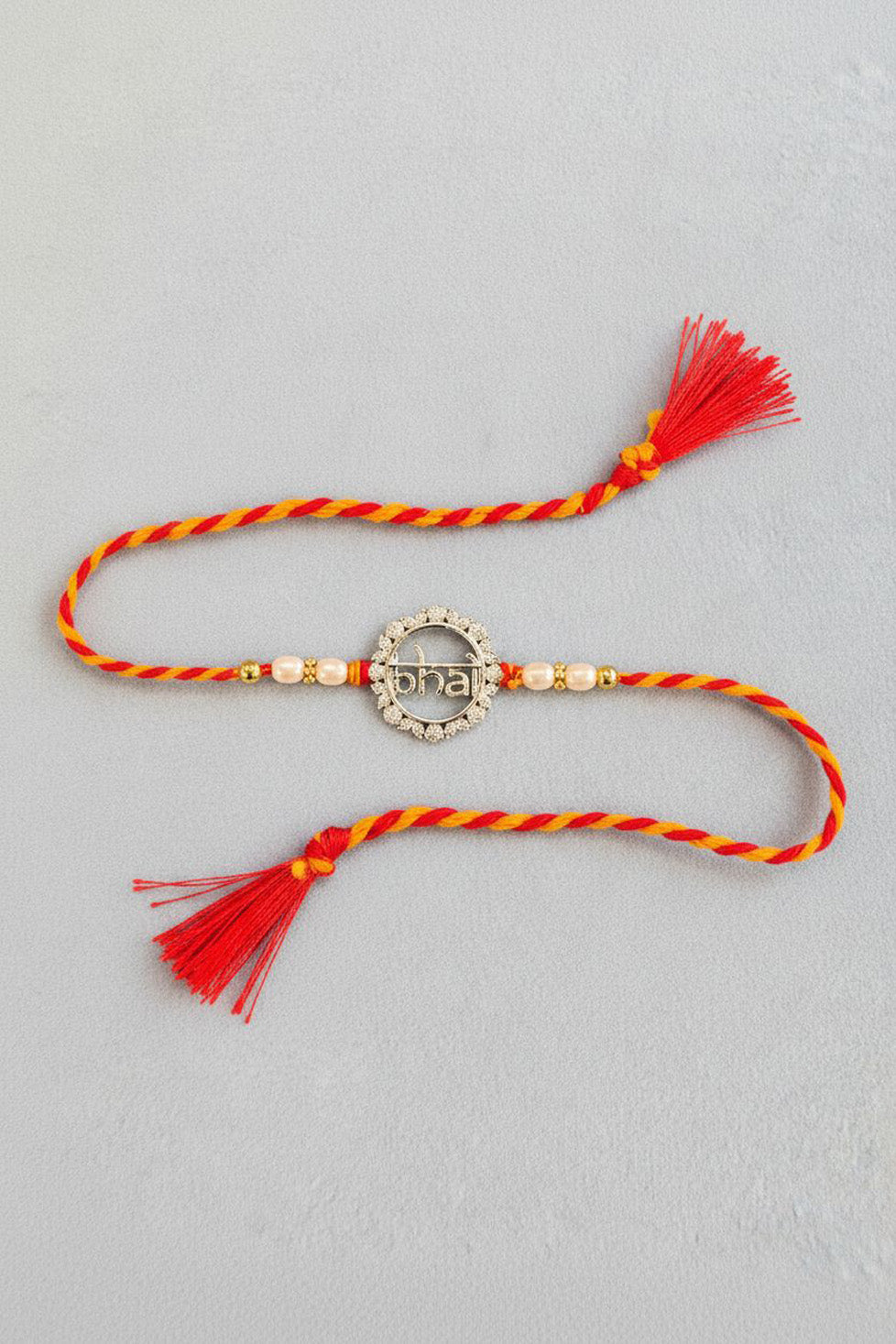 Red and orange braided rakhi with pearl beads and round silver charm, red tassels