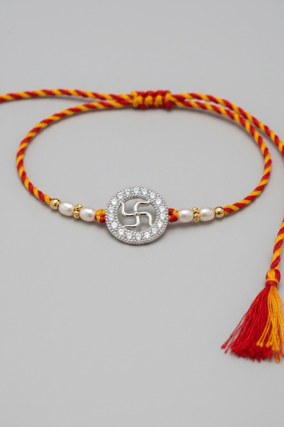 Sterling silver rakhi bracelet with circular swastik charm, pearl beads, red-yellow thread tassel