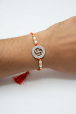 Sterling silver rakhi with circular swastik charm, pearl beads, red-yellow thread, tassel