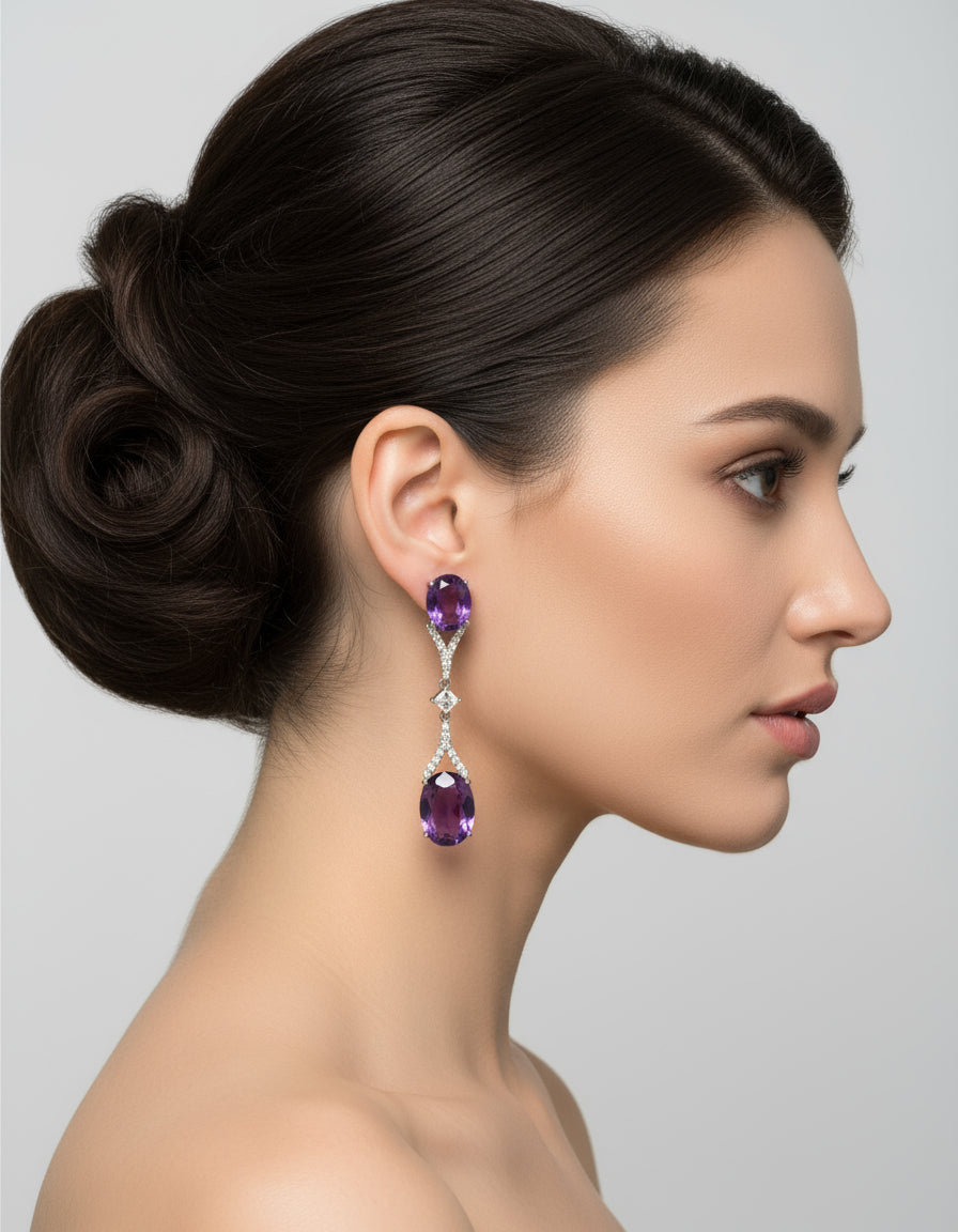 Woman wearing long silver dangle earrings with oval purple stones and delicate crystal embellishments.