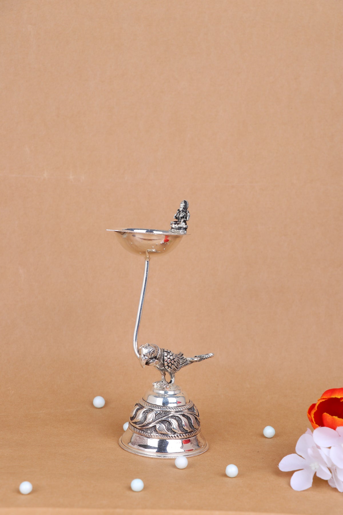 Silver-tone pooja diya lamp with shallow bowl, pedestal stem, and bird plus deity figurine