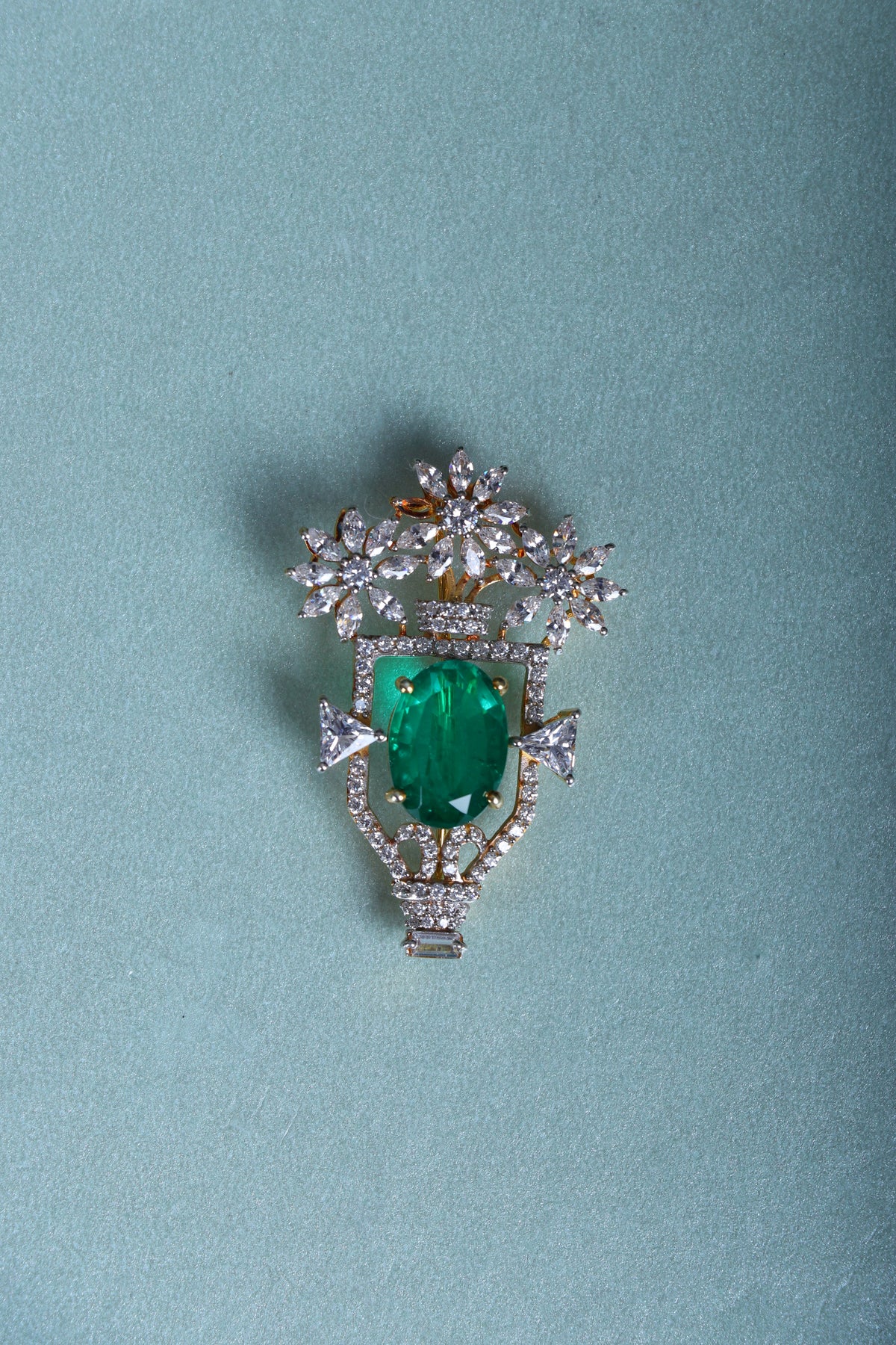 Silver brooch with green oval gemstone, floral crown setting and small drops on blue