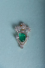 Silver brooch with green oval gemstone, floral crown setting and small drops on blue