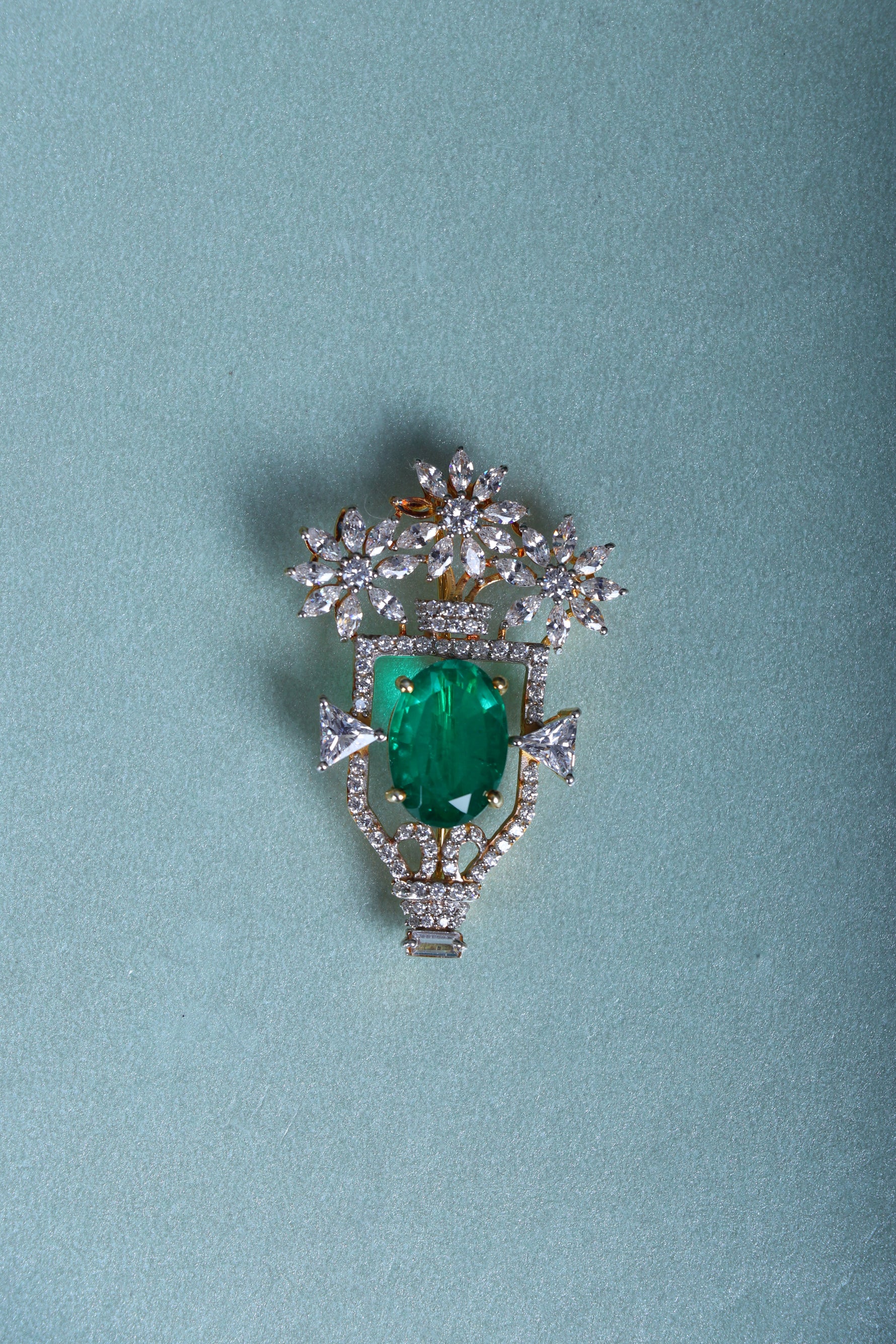 Silver brooch with green oval gemstone, floral crown setting and small drops on blue