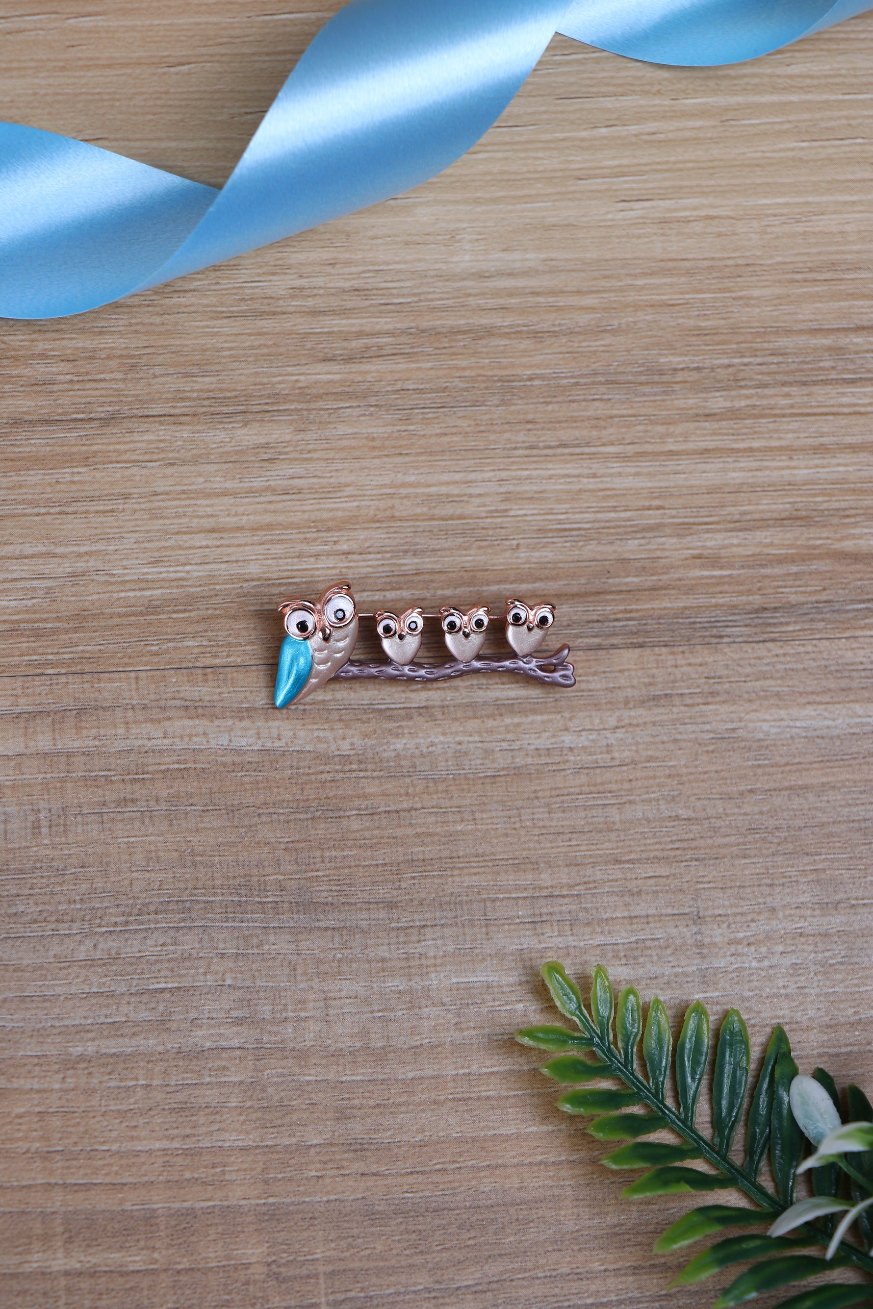 Silver-tone owl-row brooch with blue beaks on wooden tabletop