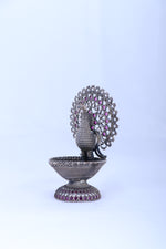 Silver-tone peacock oil diya with circular jeweled fan, purple gemstone accents