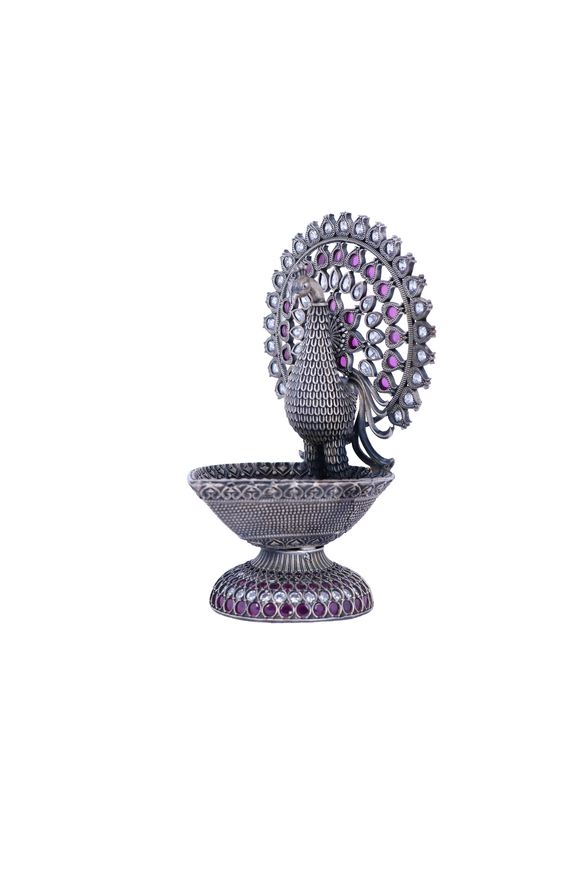 Silver-tone peacock-shaped oil diya with purple and pink gemstone inlaid details