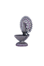 Silver-tone peacock-shaped oil diya with purple and pink gemstone inlaid details