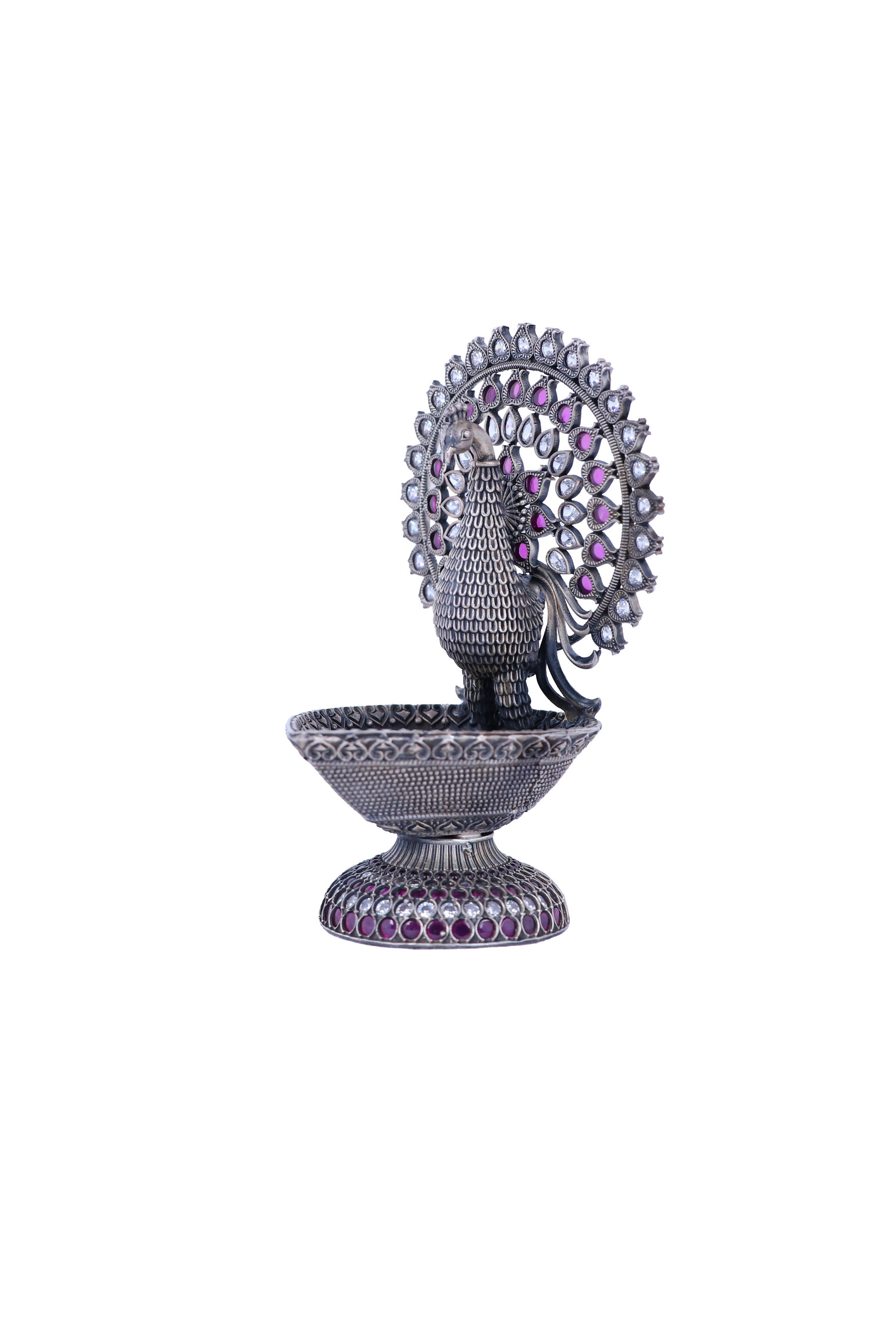 Silver-tone peacock-shaped oil diya with purple and pink gemstone inlaid details