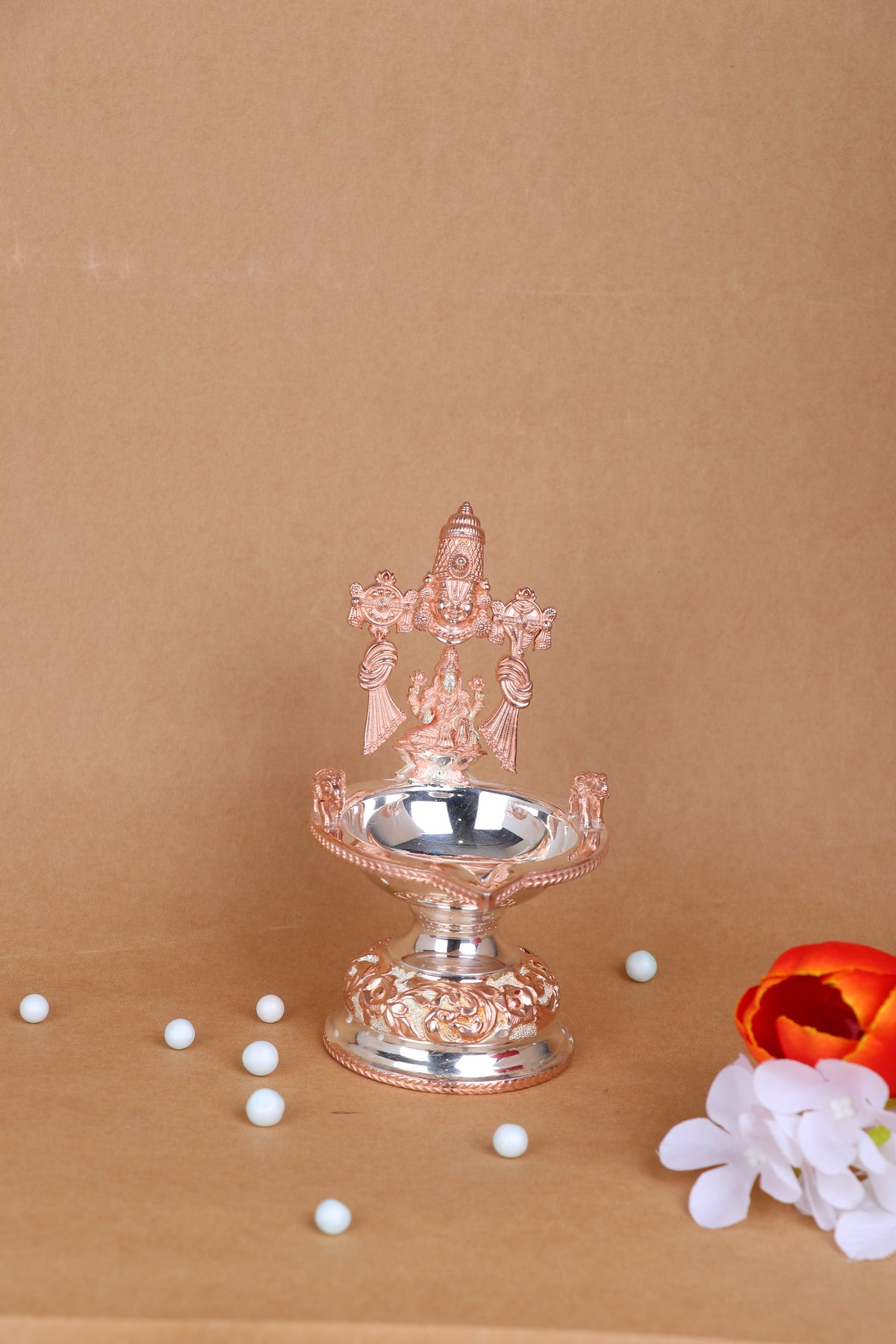 Silver-toned Lakshmi diya with prabhavali, round oil bowl on ornate pedestal; bead accents