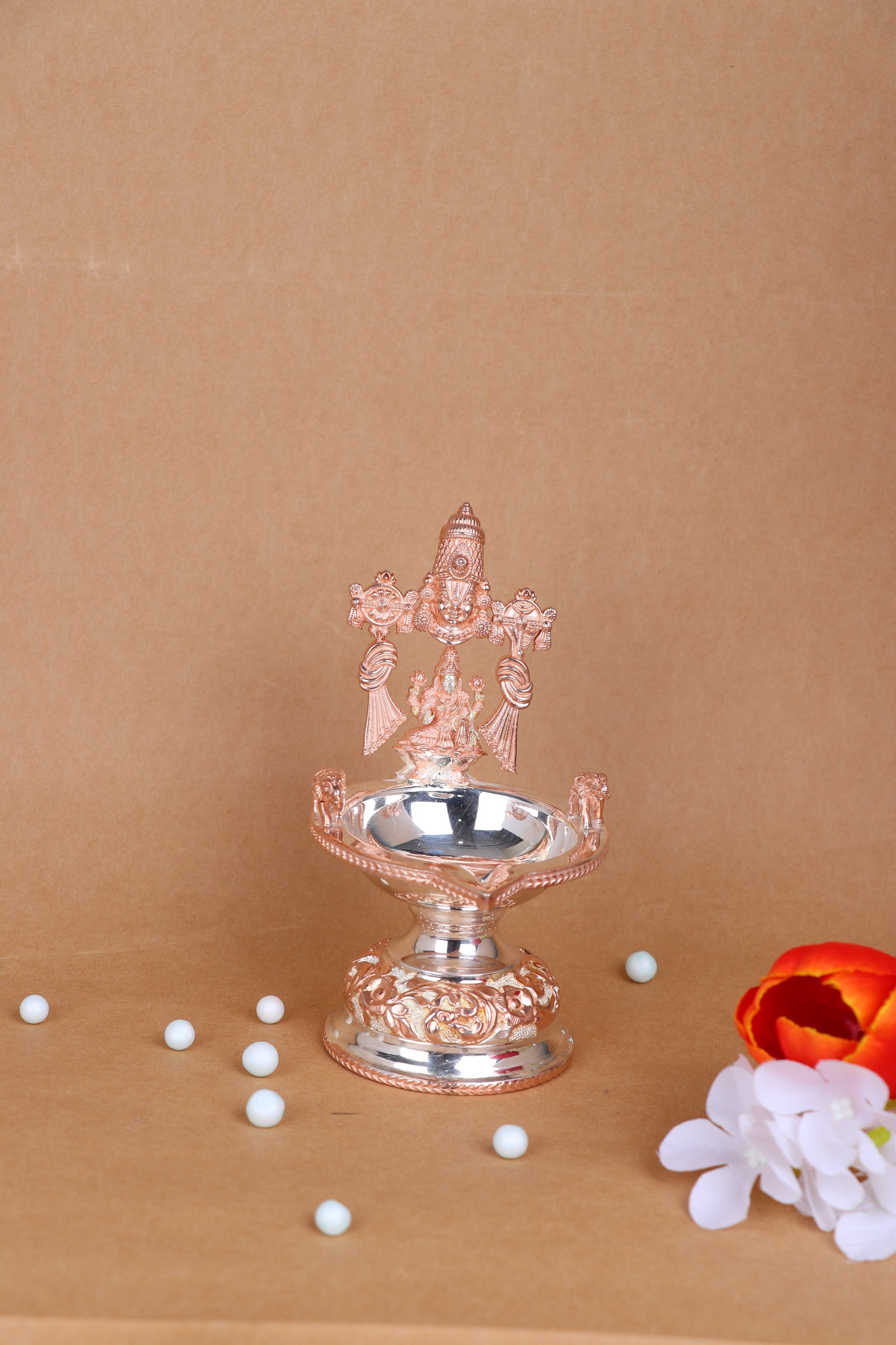 Silver-toned Lakshmi diya with prabhavali, round oil bowl on ornate pedestal; bead accents