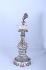 Silver peacock diya stand viewed from side with tiered body and beaded base