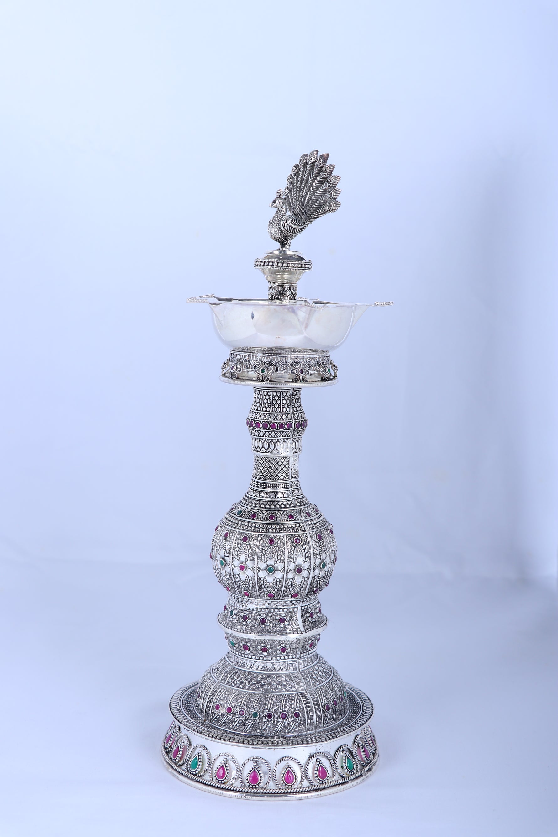 Silver peacock diya stand viewed from side with tiered body and beaded base