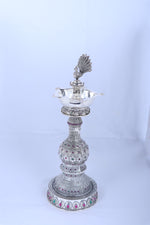 Silver peacock diya stand with flared lamp tray, detailed stem, and round base