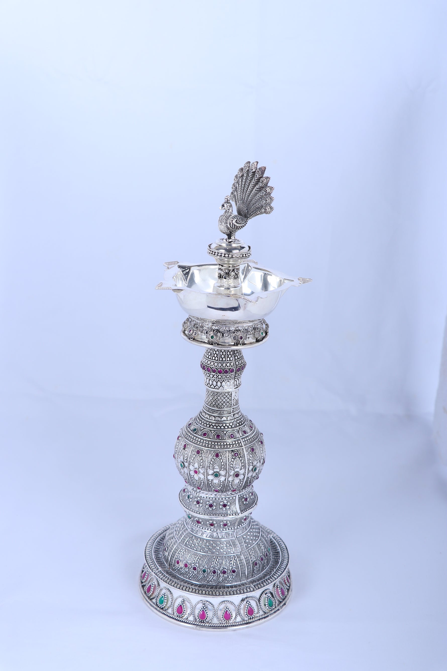Silver peacock diya stand with flared lamp tray, detailed stem, and round base
