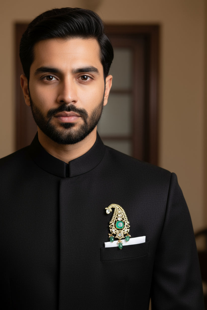 Pure silver paisley brooch with green stones and hanging pearl detail on a black sherwani.