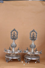 Pair of silver-tone standing temple diyas with Lakshmi relief, circular trays and claw feet