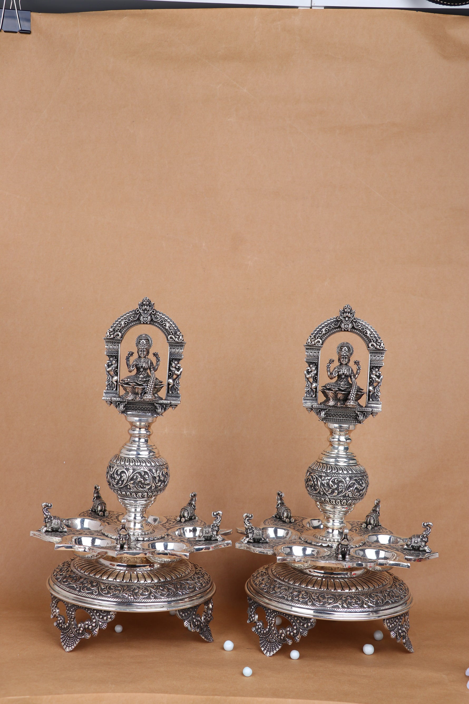 Pair of ornate silver-tone temple diyas with Lakshmi relief panels and multi-pronged trays
