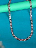 A silver chain necklace with rectangular links set with small clear stones, draped over a mint green cylindrical prop on a bright turquoise background.