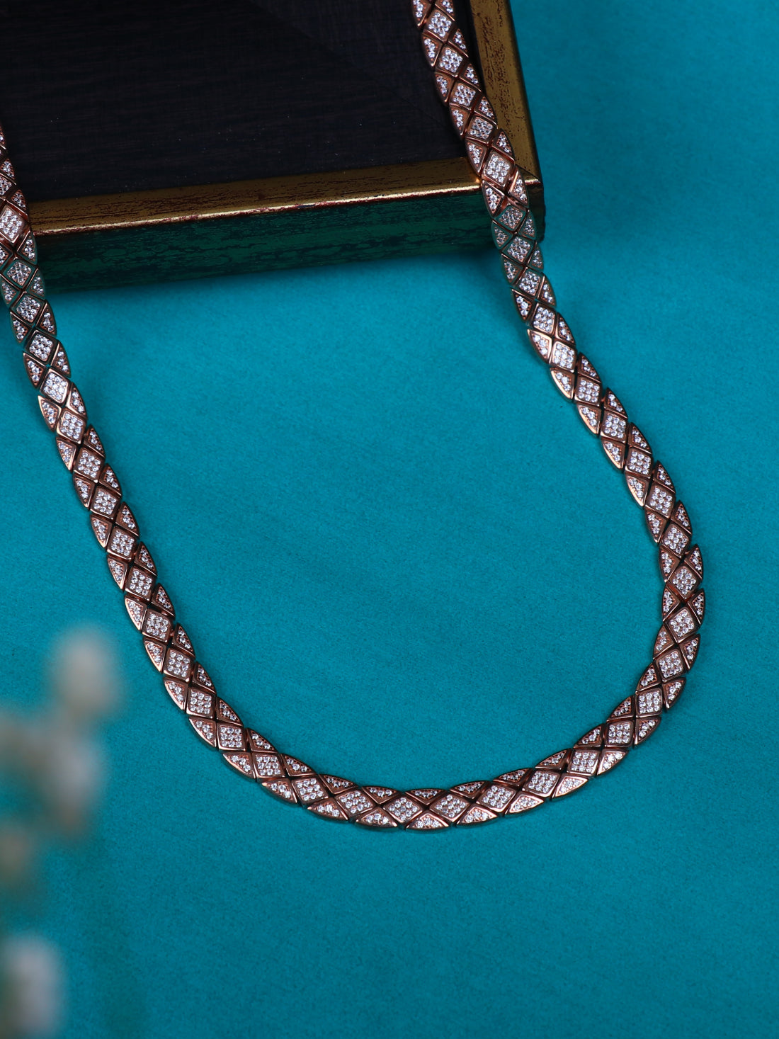 A close-up of a braided silver chain or strap with a repeating geometric pattern in brown, white, and metallic tones, arranged on a bright turquoise background.