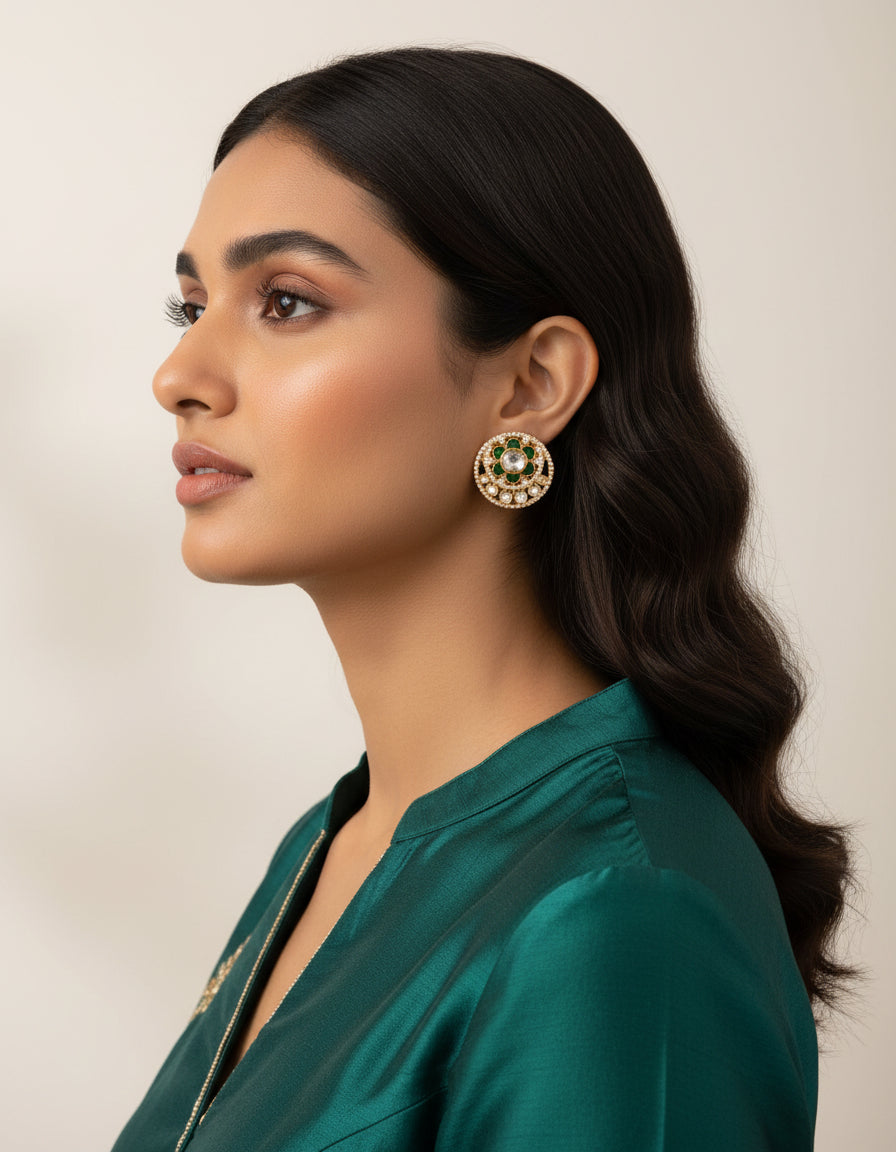 Woman wearing statement silver stud earrings with green floral accents and layered white stones.